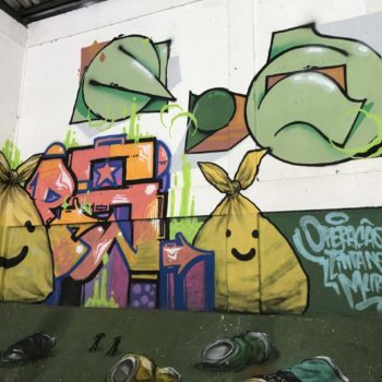Artistas: Credo, Flops, QNH e Nojon. Descrição: Continuação da Parede interna com fundo branco e verde apresenta grafitti de sacos de lixo amarelos.