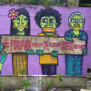 Artista: Mundano. Descrição: Parede externa roxa, apresenta grafitti com quatro pessoas, dois homens e duas mulheres, segurando uma placa que diz “parem de roubar nosso futuro”.