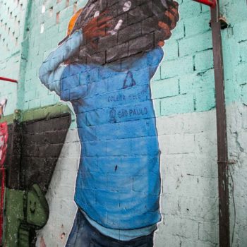 Artista: Quinho / Foto: Júlia Dávila. Descrição: Parede interna interna com grafitti de homem com uniforme da coleta seletiva da cidade. A sua cabeça é um saco de lixo.