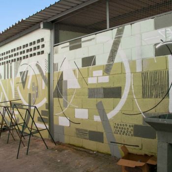 Artista: Biofa. Desccrição: Muro externo bege e branco apresenta grafitti com formas circulares de diferentes tamanhos complementadas por retângulos e quadrados, nas cores branco, cinza e marrom