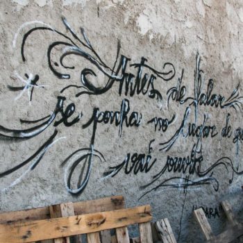 Artista: Bruno Pastore. Foto Júlia Dávila. Descrição: muro externo cinza apresenta grafitti com frase "