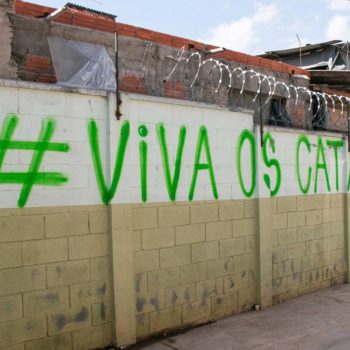 Artista: Mundano. Descrição: Muro externo apresenta grafitti em verde com a seguinte frase "hasgtag Viva os catadores"
