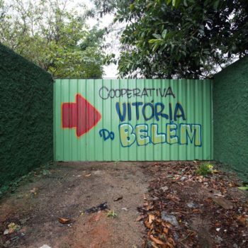 Artista Raphael Barcelos - Foto: Rebeca Figueiredo. Descrição: Portão externo verde está escrito cooperativa vitória do belém em azul.