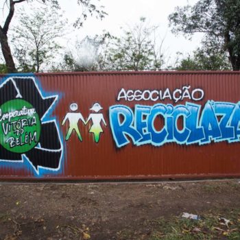 Artista: Raphael Barcelos. Foto: Rebeca Figueiredo. Descrição: portão externo com o logotipo da cooperativa Vitória de Belém e Associação Reciclazaro.
