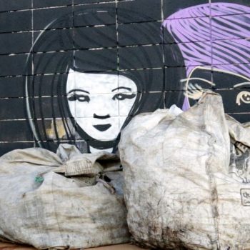 Artista: Mathiza. Descrição: Muro externo na cor preta, apresenta grafitti com desenho do contorno de dois rostos femininos, o primeiro com o cabelo preto, o segundo com cabelo roxo.