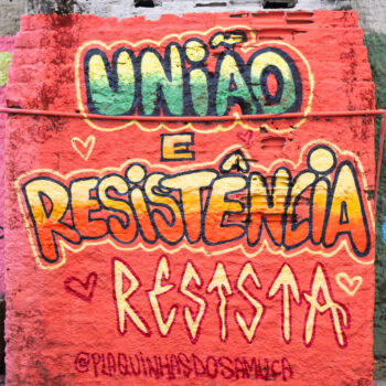 Artista: Getri | Foto: Afrovulto. Descrição - Sobre uma parede externa vermelha, em letras de formatos diferentes: “união e resistência. Resista”. “União”, em degradê de amarelo e verde; “resistência”, em degradê de amarelo ao vermelho; e “resista”, em amarelo contornado de vermelho. Abaixo, a assinatura, em vermelho. “@plaquinhasdossamuca”.